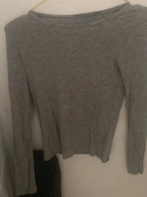Grå långärmad basic tröja - En enkel och stilren grå långärmad tröja i mjukt material. Tröjan har rund halsringning och smal passform, perfekt att bära som lager eller för en clean look. Passar till det mesta och är ett måste i garderoben.