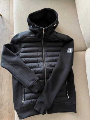 Svart cardiganjacka Alessandro Zavetti - Snygg svart cardiganjacka från Alessandro Zavetti med quiltad framsida, hög krage och dragkedja. Jackan har två fickor med dragkedja och en logotyp på ärmen. Materialmix med vadderad front och mjuka ärmar. Aldrig använd. 