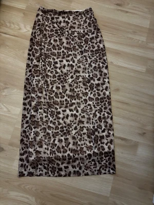 Leopardmönstrad lång kjol - Säljer en snygg lång kjol med leopardmönster i bruna och beige toner. Kjolen har rak passform och är fodrad på insidan för extra komfort. Perfekt för dig som vill sticka ut med ett djuriskt print.