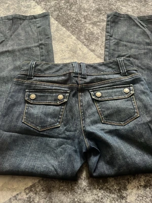 Mörkblå jeans från Ann Taylor - low waist Snygga mörkblå jeans från Ann Taylor med raka ben och dubbla knappar i midjan. köpte originalt för 1300kr.Jeansen har två bakfickor med lock och dekorativa knappar samt kontrastsömmar. Perfekta för en trendig och avslappnad stil.low waist.