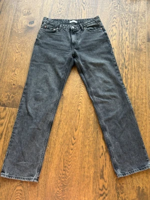 Jeans från Gina - Säljer ett par svarta raka jeans från Gina i storlek 38. Jeansen har klassisk femficksmodell, normal midja och raka ben. Materialet är denim med en tvättad look som ger en cool vintagekänsla. Perfekta till en avslappnad stil.