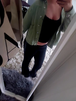 Svart croppad topp med u-ringning - Säljer en svart croppad topp med u-ringad hals och långa ärmar. Toppen har en tight passform och är perfekt att styla med jeans eller kjol. Den har en liten rosett vid halsen som även har ett fint spettsigt mönster. Enkel och stilren design som passar till många olika looks. Använd en gång så den ör som ny.