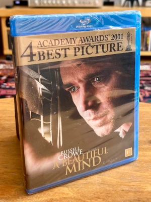 NY / INPLASTAD! A Beautiful Mind (Blu-ray) – Vinnare av 4 Oscar! - Helt ny, oöppnad och fabriksinplastad köpfilm på Blu-ray med Ron Howards fyrfaldigt Oscarsbelönade mästerverk ”A Beautiful Mind” från 2001. Filmen vann bland annat tyngsta kategorin ”Bästa film”. En gripande och helt fantastisk sann historia med Russell Crowe i sin livs roll.