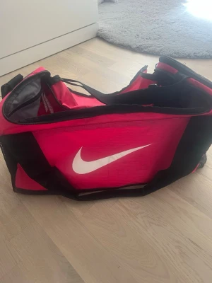 Svart, Rosa sportbag från Nike - Säljer en Svart, Rosa  sportbag från Nike med svart axelrem och vita loggan på sidan. Väskan har dragkedja upptill, flera fack och är tillverkad i slitstark syntet. Perfekt för gymmet eller träningen, rymmer mycket och är lätt att bära.