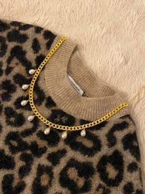 Guldhalsband med pärldetaljer - Snyggt halsband i guldfärgad metall med kedja och hängande vita pärlor. Perfekt accessoar för att lyfta din outfit med en trendig och elegant touch. Passar till många olika stilar och är lätt att matcha med andra smycken.