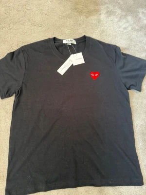 COMME Des GARCONS - Snygg och stilren T-shirt ifrån Comme des garcons, helt ny, bara provad. Säljer pga storleks fel, pefekt nu i sommar. Snygg svart med det klassiska Garcons hjärtat framtill. Pris är ej fast, slå el pling för info eller bilder!