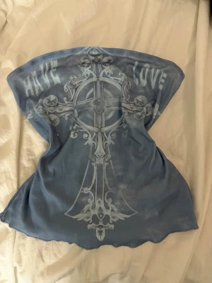 Blå tubtopp med korsmönster - Säljer en blå tubtopp med ett stort korsmönster och texten 'Have Love' framtill. Toppen är ribbad och har en bandeauform som sitter snyggt över bröstet. Perfekt för dig som vill ha en edgy och unik look.