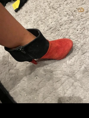 Röd och svart stövlett med klack - Snygg stövlett i rött och svart mockaimitation med hög klack och platåsula. Dragkedja på sidan för enkel påtagning och cool färgblockad design. Perfekt för dig som vill sticka ut med dina skor.