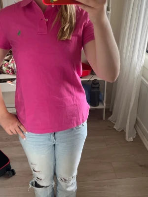 Rosa pikétröja från Ralph Lauren - Säljer en klassisk rosa pikétröja från Ralph Lauren i bomull. Tröjan har korta ärmar, krage med knappar och den ikoniska loggan broderad på bröstet. Perfekt till jeans eller shorts för en avslappnad men snygg look.
