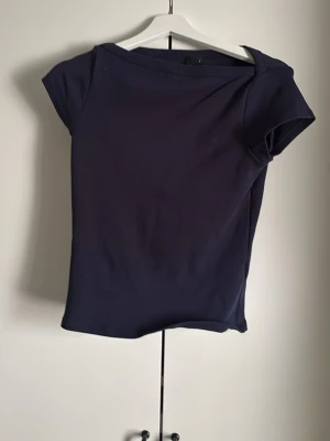 Mörkblå enkel topp med kort ärm - Snygg mörkblå topp med korta ärmar och rund halsringning. Toppen har en clean och stilren design som passar perfekt till jeans eller kjol. Materialet känns mjukt och följsamt mot kroppen.