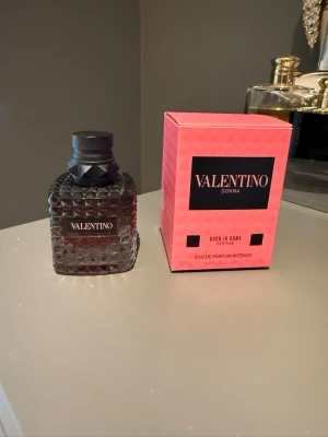 Valentino Donna Born In Roma Intense - Valentino Donna Born In Roma Intense är en lyxig parfym i en mörk, mönstrad glasflaska med svart kork. Förpackningen är rosa med svarta detaljer och tydlig logga. Flaskan har en exklusiv design som känns både modern och elegant. Innehåller 30 ml Eau de Parfum Intense. Förvarats svalt på och mörkt