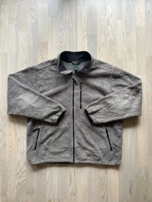 L.L.Bean fleecejacka - XL, grå - Mycket bra skick. Inga tecken på användning Jacka från L.L.Bean, storlek XL, grå Hel dragkedja, två fickor + bröstficka med dragkedja, liten krage, resår vid ärmsluten, justerbar midja, fleecekänsla Bröstvidd: 63 cm Längd: 68 cm 100% polyester Inga defekter