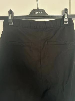 Svarta leggings med fuskfickor - Säljer ett par svarta leggings med hög midja och fuskfickor bak. De har en smal passform och är tillverkade i ett stretchigt material som sitter skönt på kroppen. Perfekta till en avslappnad look eller att styla upp med en oversized tröja.
