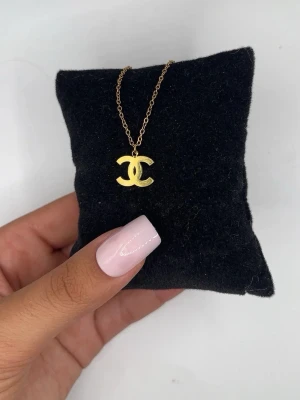 Guldigt halsband med CC-hänge - Snyggt halsband i guldfärgad metall med ett klassiskt CC-hänge. Kedjan är tunn och elegant, vilket gör att hänget verkligen står ut. Perfekt accessoar för dig som gillar stilrena och ikoniska smycken.