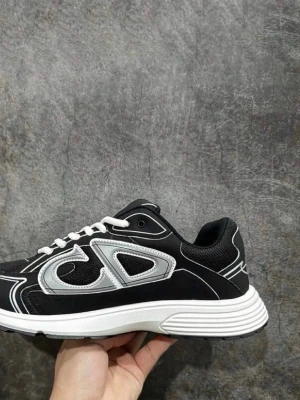 Svarta sneakers med vit sula - Stilrena svarta sneakers med vit och silverdetaljer samt vit sula. Skon har en sportig design med meshpaneler och vita skosnören. Sidan pryds av en stor silverfärgad logga och sulan är något upphöjd för extra komfort.