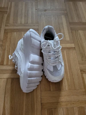 Chunky vita sneakers med mesh och mocka - Säljer ett par chunky vita sneakers med riktigt tjock sula. Ovandelen är i en mix av mesh och mockaimitation med detaljer i vitt och ljusgrått. Skorna har vita skosnören och en sportig vibe som sticker ut. Perfekta för dig som gillar statement-skor och streetstyle.