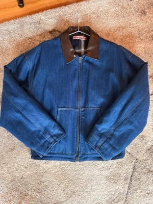Jeansjacka från Acne Studios - Snygg jeansjacka från Acne Studios i klassisk blå denim med brunt glansigt krage i kontrastmaterial. Jackan har dragkedja framtill, två stora fickor och rutigt innerfoder. Perfekt för dig som vill ha en stilren och modern look.