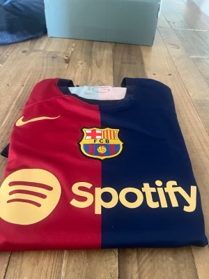 Barcelona matchtröja Nike röd/blå - Säljer en FC Barcelona matchtröja från Nike i rött och blått med klubbmärke, gul Nike-logga och Spotify som sponsortryck. Tröjan har klassisk rund hals och är tillverkad i ett lätt, ventilerande material perfekt för fotboll och träning.
