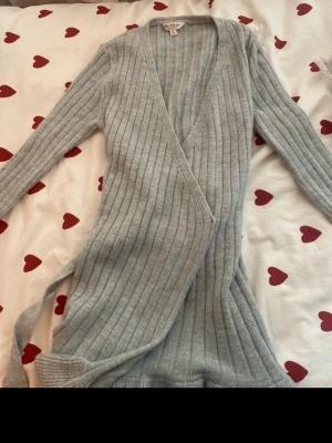 Ljusgrå ribbstickad omlottkofta - Supersnygg ljusgrå ribbstickad omlottkofta från Miss Selfridge. Koftan har långa ärmar, djup V-ringning och knytskärp i midjan. Perfekt för lager på lager och ger en chill men ändå stilren look.