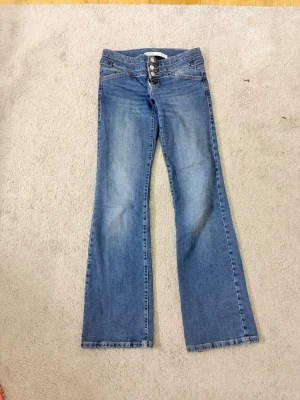 Blå bootcut jeans från Bershka - Säljer ett par blå bootcut jeans från Bershka med tre knappar i midjan och snygga sömdetaljer. Jeansen  är i bra skick. Som ni ser på bilderna, har jag sytt en del på Jeansen bredvid där man drar i dragkedjan vilket är därför Jeansen är lite billigare. Jag skulle säga att dessa jeans är xs eur 32🩵
