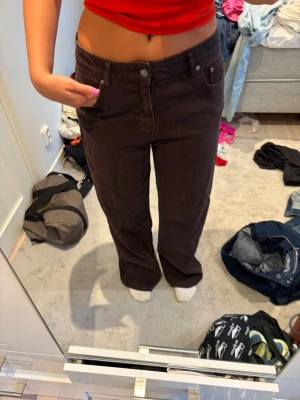 Bruna raka jeans med hög midja - Säljer ett par bruna jeans med rak passform och hög midja. Jeansen har klassiska fem fickor och stängs med knapp och dragkedja. Materialet ser ut att vara bomullsdenim med en mjuk finish. Perfekta för en avslappnad och trendig look.