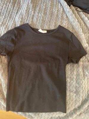Svart basic t-shirt Gina Tricot XS - En svart basic t-shirt från Gina Tricot i modellen basically basics. T-shirten har rund halsringning och korta ärmar. Tillverkad i mjuk bomull som är skön mot huden. Perfekt att matcha med jeans eller kjol för en enkel och clean look.