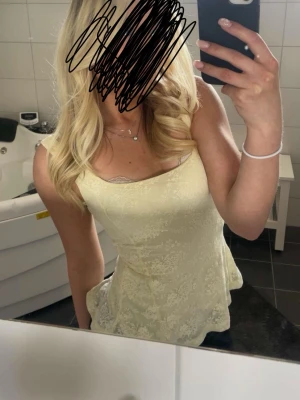 Ljusgul spetsdetaljerad linnetopp - Söt ljusgul linnetopp med tunna axelband och spetsdetaljer vid urringningen. Toppen har en lätt utsvängd passform och är perfekt för varma dagar. Materialet ser ut att vara mjukt och luftigt, vilket ger en bekväm känsla. Från Gina tricot. 