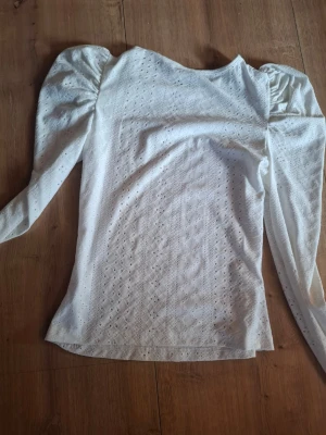 Vit topp med puffärm från SHEIN - Säljer en vit topp från SHEIN i storlek S med puffärmar och broderie anglaise-mönster. Toppen har rund halsringning och är gjord i ett lätt, luftigt material som känns fräscht och trendigt. Perfekt för dig som gillar romantisk och feminin stil.