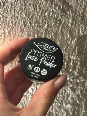 puroBIO PR1MER Loose Powder - puroBIO PR1MER Loose Powder är ett transparent löspuder i en liten rund burk. Pudret är veganskt, ekologiskt och nickeltestat, perfekt för att matta ner huden och ge en jämn bas. Förpackningen är svart med vit text och innehåller 5g.