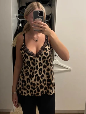 Leopardmönstrad linnetopp med spets - Snygg leopardmönstrad linnetopp med tunna axelband och v-ringning dekorerad med svart spets. Perfekt för dig som vill sticka ut och addera lite edge till din outfit. Lätt och luftig känsla.