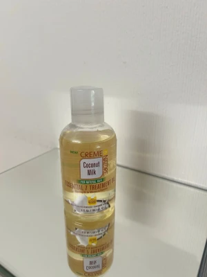 Creme of Nature Coconut Milk olja - Behandlingsolja för hår från Creme of Nature med kokosmjölk. Kommer i en genomskinlig plastflaska med vit kork och gul etikett. Oljan är ljusgul och passar för naturligt hår. Perfekt för att ge näring och glans.