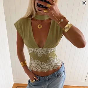 Grön korsettopp med spetsdetaljer - Trendig grön korsettopp med djup v-ringning och breda axlar. Toppen har vackra vita spetsdetaljer med blommönster över midjan och en matchande choker runt halsen. Perfekt för dig som vill sticka ut med en unik och snygg topp. Storlek s💓💓