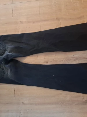 Svarta bootcut jeans med slitningar - Säljer ett par svarta bootcut jeans med snygga slitningar och tvättade detaljer på låren. Jeansen har klassisk femficksdesign och raka ben som går ut något nedtill. Perfekta för dig som gillar en avslappnad men trendig stil.