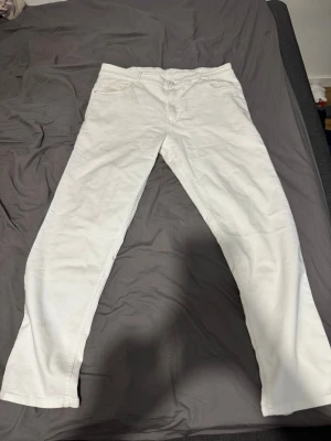 Vita raka jeans - Säljer ett par vita jeans med rak passform och klassisk femficksdesign. Jeansen har normal midja och stängs med dragkedja och knapp. Perfekta för dig som vill ha en clean och stilren look.