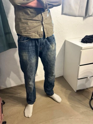 Blå jeans från Denim & Supply Ralph Lauren - Säljer ett par blå jeans från Denim & Supply Ralph Lauren med slitna detaljer och tvättad look. Klassisk femficksmodell med normal passform och snygga kontrastsömmar. Perfekta för dig som gillar en avslappnad och trendig stil.