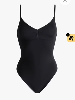 Svart body med smala axelband - Snygg svart body med smala axelband och lätt rynkning vid bysten. Kroppsnära passform och mjukt, stretchigt material som ger en clean och stilren look. Perfekt att styla under skjortor eller tröjor för en enkel och trendig outfit.