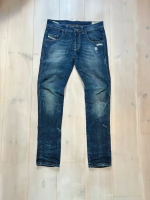 Mörkblå slim fit jeans med slitningar - Snygga mörkblå jeans i slim fit-modell med tydliga slitningar och ljusare partier på framsidan. Klassisk femficksdesign och låg midja. Jeansen har en modern tvätt och detaljer som ger en cool, använd look.