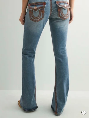 Blå bootcut jeans med kontrastsömmar - True religion jeans som endast har använts max 3-4ggr max. Men eftersom dem har varit för långa har de fått små hål och defekter längst ner byxorna (bild på defekterna finns). Defekerna syns inte alls tydligt när man har på sig byxorna ( variera på ens längd) själv är jag runt 163cm. Förutom defekterna är byxorna i ett bra skick.
