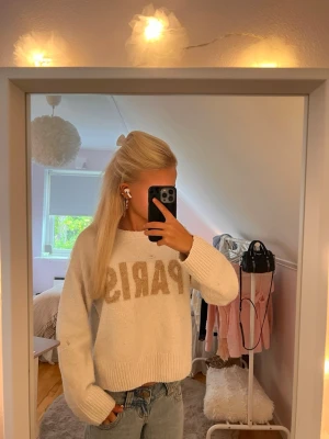 Vit stickad tröja med PARIS-tryck - Mysig vit stickad tröja med stora bokstäver 'PARIS' i beige framtill. Tröjan är från h&m och är i storlek S. Den är perfekt för en basic outfit på hösten🤎. Inga stora effekter utan lite nopprig men inget som syns🥰