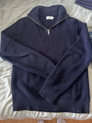 Mörkblå stickad tröja med halvzip - Snygg mörkblå stickad tröja från East West med halvzip och hög krage. Tröjan har långa ärmar, ribbstickade muddar och är gjord i ett mjukt, grovt stickat material. Perfekt för lager på lager och en stilren look.