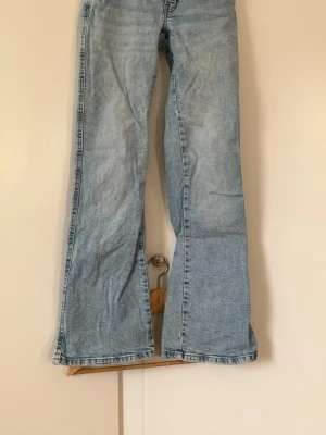 Ljusblå bootcut jeans 157 - Säljer ett par ljusblå bootcut jeans från 157 med klassisk femficksmodell och dubbla silverknappar i midjan. Jeansen har en avslappnad passform och är tillverkade i denim med snygg tvätt. Perfekta för en trendig och avslappnad stil.