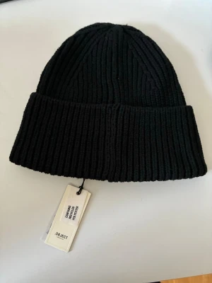 Svart ribbstickad mössa från OBJECT - Säljer en svart ribbstickad mössa från OBJECT med bred uppvikt kant. Klassisk modell i mjukt material som passar perfekt till kalla dagar. Enkel och stilren design som funkar till det mesta.