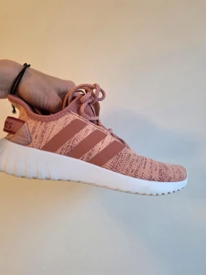 Rosa Adidas sneakers med stickad ovandel - Säljer ett par snygga rosa Adidas sneakers med stickad ovandel och klassiska tre ränder på sidan. Skorna har vita sulor och matchande rosa skosnören. Perfekta för dig som gillar sportig och trendig stil.