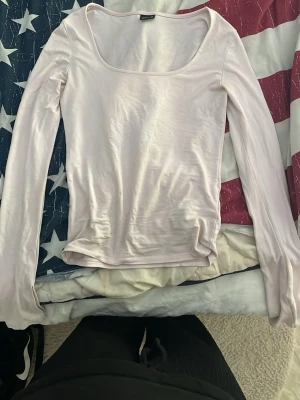 Ljusrosa långärmad topp med rundringning - En enkel och stilren ljusrosa långärmad topp med bred rundringning. Tillverkad i ett mjukt och stretchigt material som ger en bekväm passform. Perfekt att matcha med jeans eller kjol för en clean look.