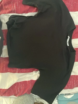 Svart omlottopp med knytband - Snygg svart omlottopp med långa ärmar och knytband i midjan. Toppen har en enkel, stilren design och är gjord i ett mjukt, stretchigt material som sitter skönt på kroppen. Perfekt att matcha med både jeans och kjol för en trendig look.