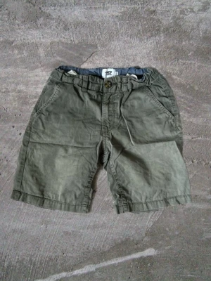 Olivgröna bomullsshorts med fickor - Snygga olivgröna shorts i bomull med klassisk passform. Shortsen har två sidofickor fram och två bakfickor, samt hällor för bälte. Perfekta för varma dagar och enkel att matcha med t-shirt eller skjorta.
