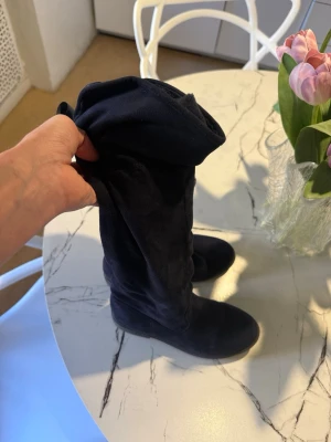 Svarta overknee stövlar i mockaimitation - Säljer ett par svarta overknee stövlar i mjuk mockaimitation. De har rund tå och låg klack, perfekt för en trendig look. Stövlarna är flexibla och kan vikas ner för olika stilar. Passar till både jeans och kjol.