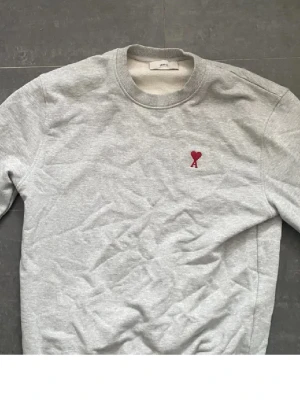 Grå sweatshirt från Ami - Säljer denna tröjan från Ami Paris i Storlek M. Använd en gång så den är i nyskick,  Inköpt från care of Carl , Säljer denna för 800 