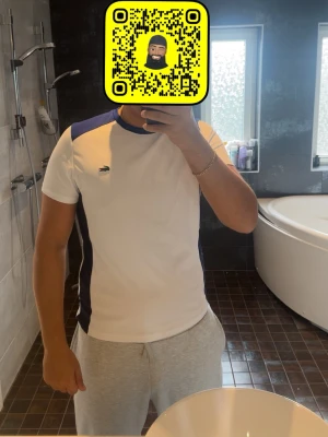 Vit och blå Lacoste t-shirt äkta sällsynt!! - Säljer en vit t-shirt från Lacoste med blå detaljer på axlar och sidor. T-shirten har grönt Lacoste-tryck och krokodil på ryggen samt liten krokodillogo fram. Klassisk rund hals och korta ärmar. Perfekt för en sportig och clean look. Sällsynt omöjligt hitta idag! Äkta Lacoste 