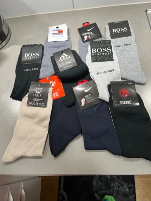 Mix av märkesstrumpor i olika färger märkes strl 41-49 nya - Säljer ett paket med flera par strumpor från Hugo Boss, Nike, Adidas, Emporio Armani och Diesel. Strumporna kommer i färgerna svart, grå, beige, marinblå och mörkblå. Klassisk design, perfekta till vardags. Materialet är främst bomull och polyester.